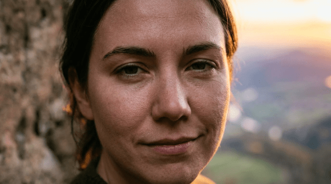 Person sitting inside stone structure looking at sunset over river and mountains